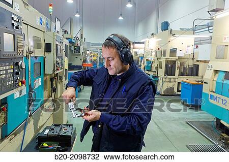 Stock Image - Worker measuring with caliper. Area automated CNC lathes. Machined Indecober. Machining of precision parts in series. Automotive industry. Berriz. Bizkaia. Basque Country. Spain.. Fotosearch