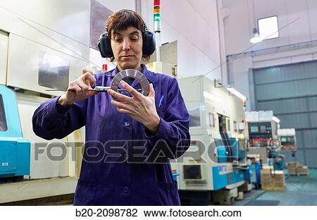 Stock Image - Worker measuring with caliper. Area automated CNC lathes. Machined Indecober. Machining of precision parts in series. Automotive industry. Berriz. Bizkaia. Basque Country. Spain.. Fotosearch
