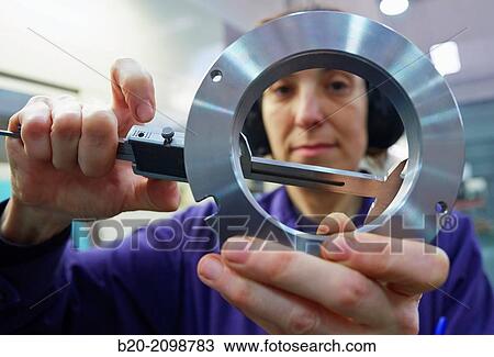 Stock Image - Worker measuring with caliper. Area automated CNC lathes. Machined Indecober. Machining of precision parts in series. Automotive industry. Berriz. Bizkaia. Basque Country. Spain.. Fotosearch