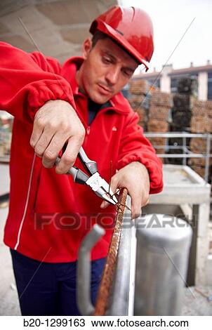 Stock Image - Worker using pliers in construction site, preparing concrete rods. Fotosearch