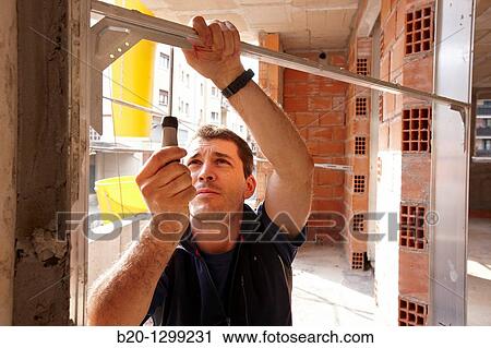 Stock Image - Worker using screwdriver, assembling window frame, new homes under construction, construction site. Fotosearch