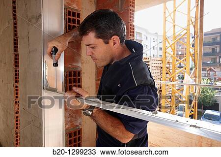 Stock Image - Worker using screwdriver, assembling window frame, new homes under construction, construction site. Fotosearch
