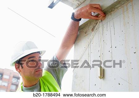 Picture - Worker with protective equipment, PPE, Checking and aligning vertical sections in concrete walls, housing construction, Plumb line, Basque Country, Spain. Fotosearch