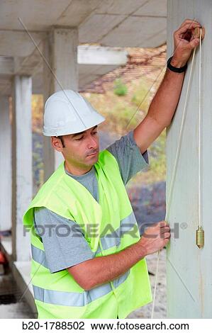 Stock Image - Worker with protective equipment, PPE, Checking and aligning vertical sections in concrete walls, housing construction, Plumb line, Basque Country, Spain. Fotosearch