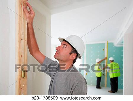 Stock Photo - Worker with protective equipment, PPE, Checking and aligning vertical sections in preframe door, housing construction, Plumb line, Basque Country, Spain. Fotosearch