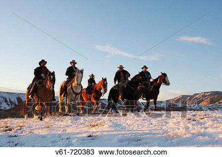 Stock Image - Wranglers leading their horses over the snowcaped ranges of wyoming at sunset. Fotosearch