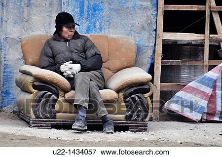 Yangshou (China): a man sitting on a couch along a sidewalk, at the bottom of a building construction View Large Photo Image Stock Photo - Yangshou (China): a man sitting on a couch along a sidewalk, at the bottom of a building construction. Fotosearch