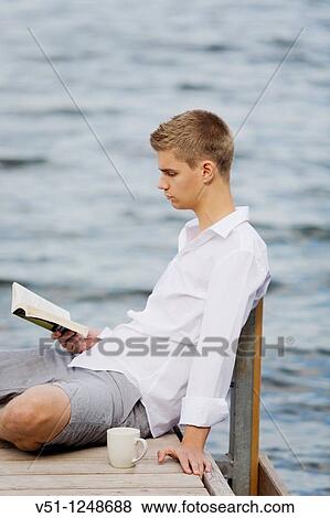 Stock Photo - Youn man reading a book with a coffee in a pier by the sea. Fotosearch