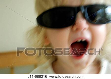 Stock Photograph - Young 1 one year old baby girl wearing black sunglasses fooling around playing on holiday. Fotosearch
