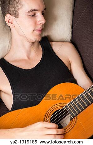 Young adult male relaxing and playing on his acoustic guitar View Large Photo Image Stock Photography - Young adult male relaxing and playing on his acoustic guitar. Fotosearch