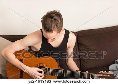 Young adult male sit in sofa and practice on his acoustic guitar View Large Photo Image Stock Image - Young adult male sit in sofa and practice on his acoustic guitar. Fotosearch