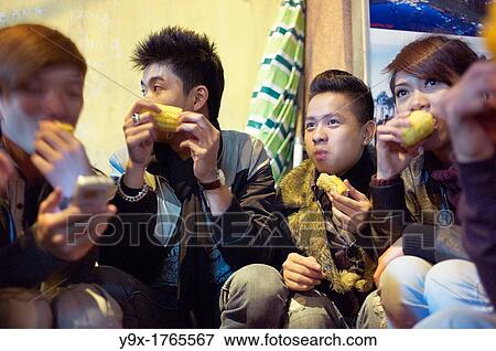 Young adults eating corn on the streets of Vietnam at night View Large Photo Image Stock Photo - Young adults eating corn on the streets of Vietnam at night. Fotosearch