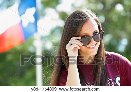Stock Photo - Young american female teenager of 17 years peeking over her sun glasses with Texas flag in the background. Fotosearch