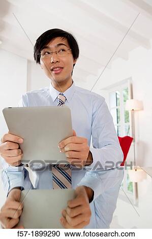 Young Asian businessman communicating on his Tablet computer View Large Photo Image Stock Image - Young Asian businessman communicating on his Tablet computer. Fotosearch