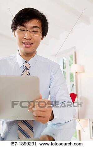 Young Asian businessman communicating on his Tablet computer View Large Photo Image Stock Image - Young Asian businessman communicating on his Tablet computer. Fotosearch