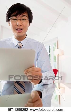 Young Asian businessman communicating on his Tablet computer View Large Photo Image Stock Image - Young Asian businessman communicating on his Tablet computer. Fotosearch