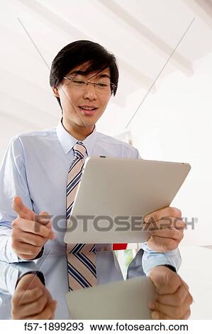 Young Asian businessman communicating on his Tablet computer View Large Photo Image Stock Image - Young Asian businessman communicating on his Tablet computer. Fotosearch