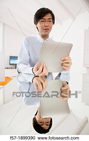 Young Asian businessman communicating on his Tablet computer View Large Photo Image Stock Image - Young Asian businessman communicating on his Tablet computer. Fotosearch