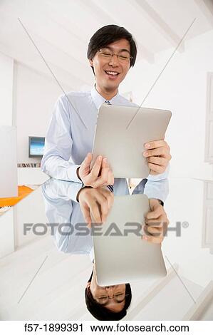 Young Asian businessman communicating on his Tablet computer View Large Photo Image Stock Image - Young Asian businessman communicating on his Tablet computer. Fotosearch