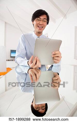 Stock Photo - Young Asian businessman communicating on his Tablet computer. Fotosearch