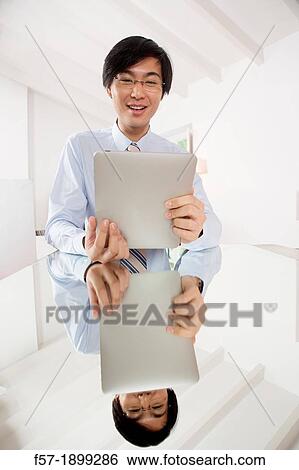 Young Asian businessman communicating on his Tablet computer View Large Photo Image Stock Photograph - Young Asian businessman communicating on his Tablet computer. Fotosearch