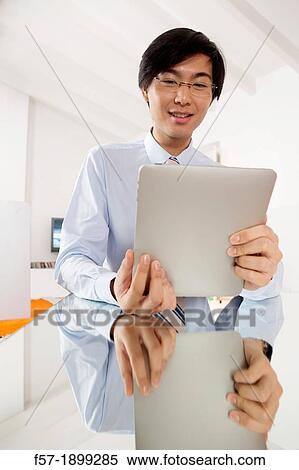 Young Asian businessman communicating on his Tablet computer View Large Photo Image Stock Photography - Young Asian businessman communicating on his Tablet computer. Fotosearch