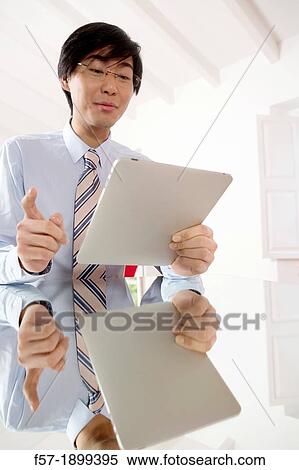 Stock Photography - Young Asian businessman communicating on his Tablet computer. Fotosearch