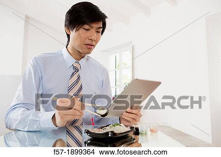 Young Asian businessman eating sushi while communicating on his Tablet computer View Large Photo Image Picture - Young Asian businessman eating sushi while communicating on his Tablet computer. Fotosearch