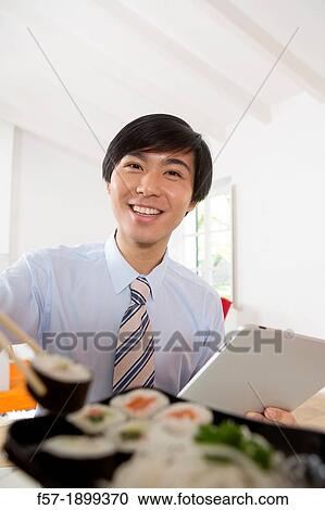 Young Asian businessman eating sushi while communicating on his Tablet computer View Large Photo Image Stock Image - Young Asian businessman eating sushi while communicating on his Tablet computer. Fotosearch