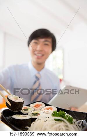Young Asian businessman eating sushi while communicating on his Tablet computer View Large Photo Image Stock Photo - Young Asian businessman eating sushi while communicating on his Tablet computer. Fotosearch