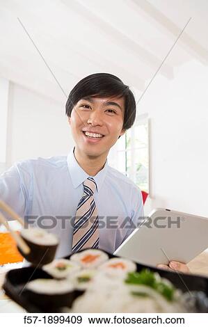 Young Asian businessman eating sushi while communicating on his Tablet computer View Large Photo Image Stock Photo - Young Asian businessman eating sushi while communicating on his Tablet computer. Fotosearch