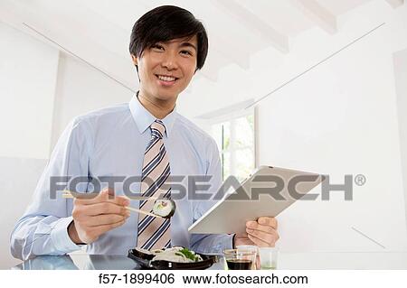 Young Asian businessman eating sushi while communicating on his Tablet computer View Large Photo Image Stock Photograph - Young Asian businessman eating sushi while communicating on his Tablet computer. Fotosearch