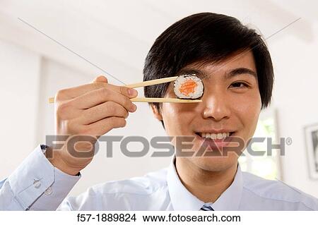 Young Asian businessman holding sushi in his chopsticks View Large Photo Image Picture - Young Asian businessman holding sushi in his chopsticks. Fotosearch