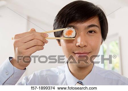 Young Asian businessman holding sushi in his chopsticks View Large Photo Image Picture - Young Asian businessman holding sushi in his chopsticks. Fotosearch