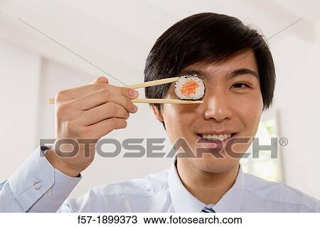 Young Asian businessman holding sushi in his chopsticks View Large Photo Image Stock Image - Young Asian businessman holding sushi in his chopsticks. Fotosearch