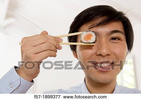 Young Asian businessman holding sushi in his chopsticks View Large Photo Image Stock Photo - Young Asian businessman holding sushi in his chopsticks. Fotosearch