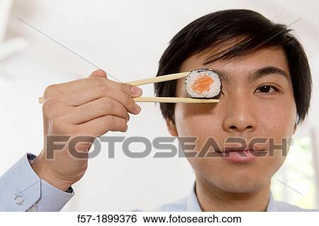 Young Asian businessman holding sushi in his chopsticks View Large Photo Image Stock Photograph - Young Asian businessman holding sushi in his chopsticks. Fotosearch