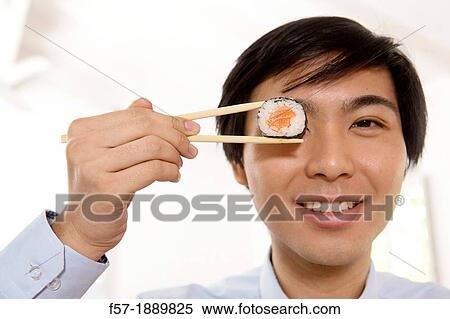 Young Asian businessman holding sushi in his chopsticks View Large Photo Image Stock Photography - Young Asian businessman holding sushi in his chopsticks. Fotosearch