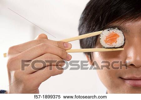Stock Photography - Young Asian businessman holding sushi in his chopsticks. Fotosearch