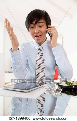 Stock Image - Young Asian businessman talking on his smartphone. Fotosearch