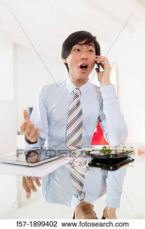 Stock Image - Young Asian businessman talking on his smartphone. Fotosearch