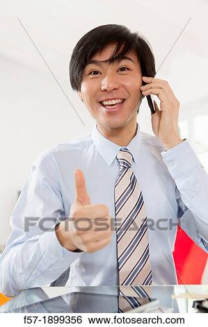 Young Asian businessman talking on his smartphone View Large Photo Image Stock Photograph - Young Asian businessman talking on his smartphone. Fotosearch