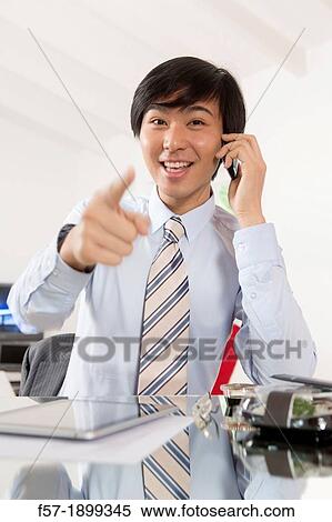 Stock Photography - Young Asian businessman talking on his smartphone. Fotosearch
