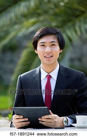 Young Asian businessman using his Tablet computer outside View Large Photo Image Picture - Young Asian businessman using his Tablet computer outside. Fotosearch