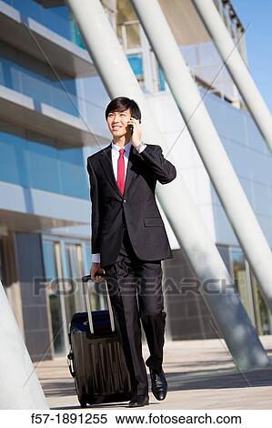 Young Asian businessman walking from the terminal on his smartphone View Large Photo Image Stock Photography - Young Asian businessman walking from the terminal on his smartphone. Fotosearch