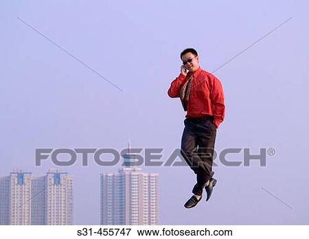 Young Asian (Chinese) Businessman caught in mid-air, talking on a cell phone; ground not visible, hi-rise buildings in the background View Large Photo Image Stock Photo - Young Asian (Chinese) Businessman caught in mid-air, talking on a cell phone; ground not visible, hi-rise buildings in the background. Fotosearch