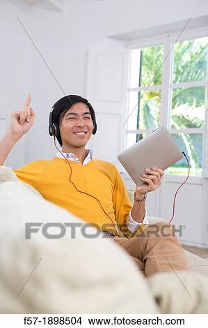 Young Asian man using his Tablet computer View Large Photo Image Picture - Young Asian man using his Tablet computer. Fotosearch