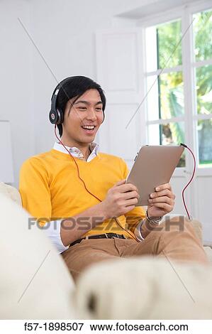 Stock Photo - Young Asian man using his Tablet computer. Fotosearch