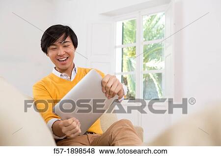 Young Asian man using his Tablet computer View Large Photo Image Stock Photo - Young Asian man using his Tablet computer. Fotosearch