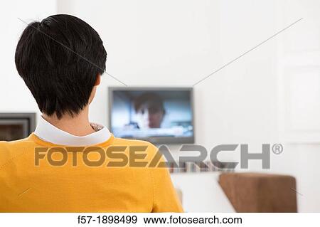 Stock Photo - Young Asian man watching TV. Fotosearch